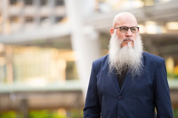 Зрелый бородатый лысый бизнесмен думает в городе на открытом воздухе — стоковое фото
