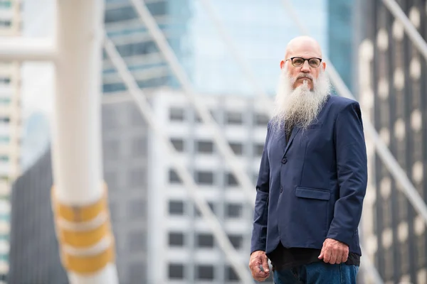 Зрелый бородатый лысый бизнесмен думает в городе на открытом воздухе — стоковое фото