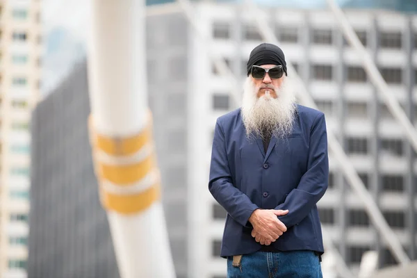 Зрелый бородатый бизнесмен в солнцезащитных очках и шапочках на улице города — стоковое фото
