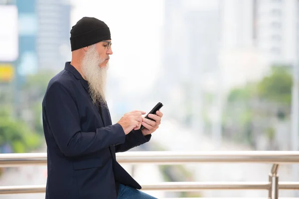 Profile view of mature bearded businessman using phone in the city outdoors — Stock Photo, Image