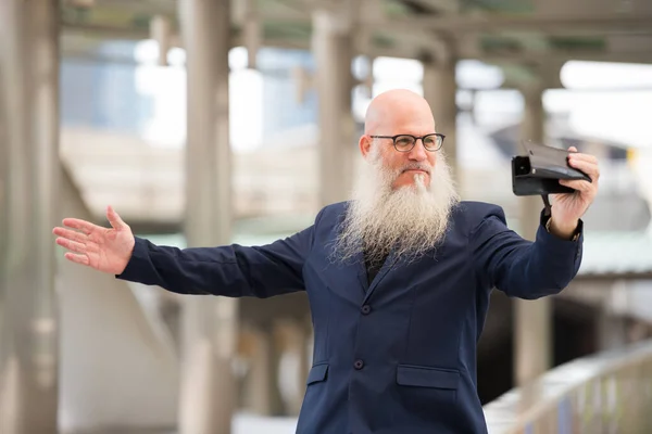 Volwassen bebaarde kale zakenman vlogging met telefoon in de stad buiten — Stockfoto