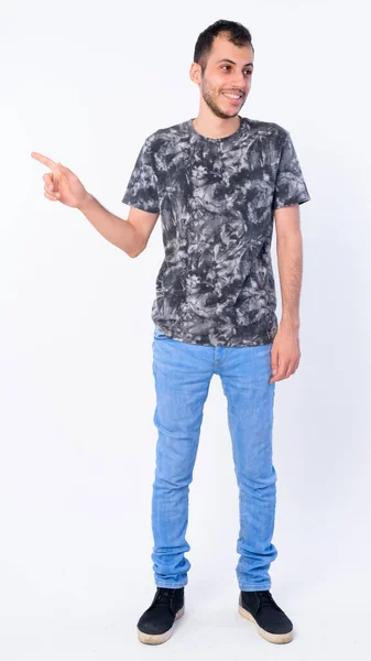 Full body shot of happy young bearded Persian man pointing finger and looking away — Stock Photo, Image