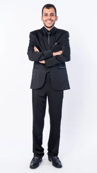 Full body shot of happy young bearded Persian businessman in suit smiling with arms crossed — Stock Photo, Image