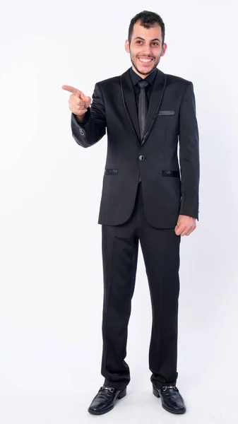 Πλήρης πυροβολισμό σώμα του χαρούμενος νεαρός γενειοφόρος Πέρσης επιχειρηματίας με κοστούμι δείχνοντας δάχτυλο — Φωτογραφία Αρχείου