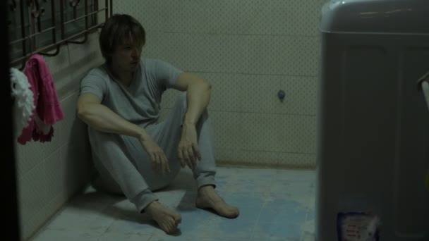 Bote de cuerpo completo de joven desaliñado sentado en el suelo de la habitación espeluznante oscuro — Vídeo de stock