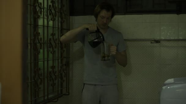 Зневірений молодий чоловік п'є каву в темній моторошній кімнаті — стокове відео