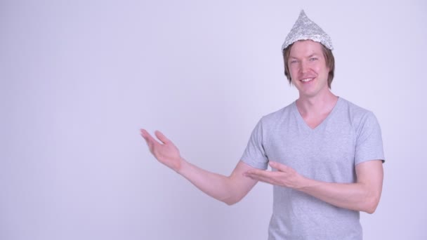 Joven feliz con sombrero de papel de aluminio mostrando algo — Vídeos de Stock