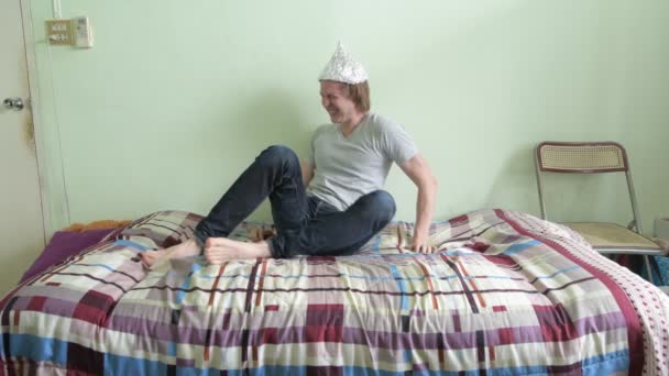 Joven estresado con sombrero de papel de aluminio y asustado en el dormitorio — Vídeo de stock