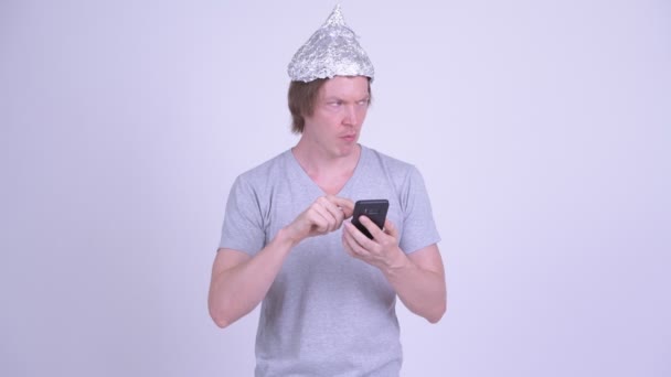 Młody człowiek w kapeluszu z folii aluminiowej za pomocą telefonu — Wideo stockowe