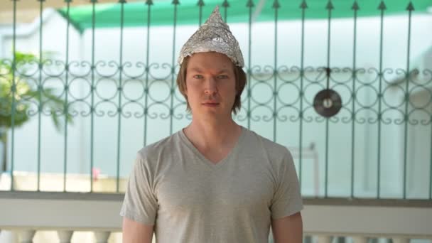Gelukkige jongeman draagt tinnen folie hoed als complottheorie concept buiten — Stockvideo