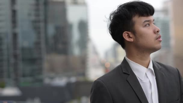 Portrait of young Asian businessman against view of the city — Stockvideo