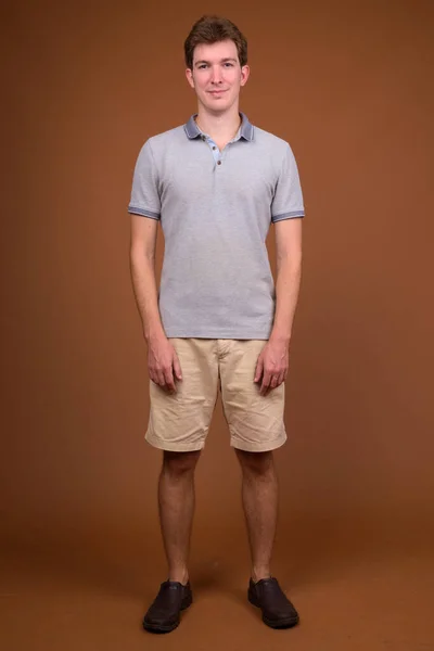 Fiatal jóképű férfi szürke inget visel barna háttér — Stock Fotó
