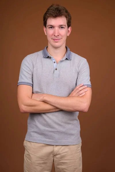 Fiatal jóképű férfi szürke inget visel barna háttér — Stock Fotó