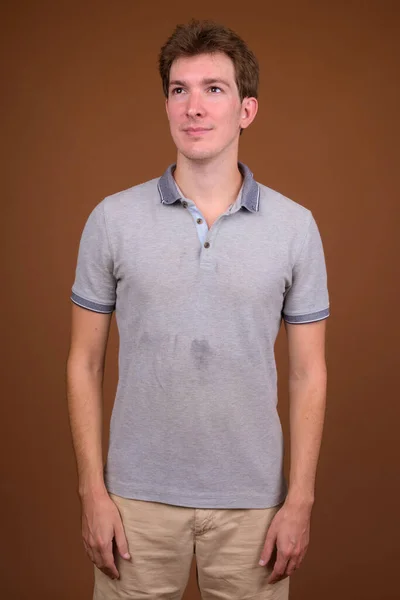Молодой красивый мужчина в серой рубашке на коричневом фоне — стоковое фото