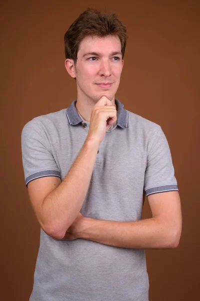 Junger schöner Mann mit grauem Hemd vor braunem Hintergrund — Stockfoto