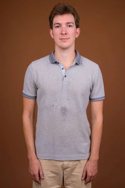 Pemuda tampan mengenakan kemeja abu-abu terhadap latar belakang coklat — Stok Foto