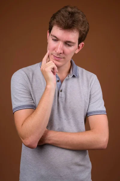 Junger schöner Mann mit grauem Hemd vor braunem Hintergrund — Stockfoto