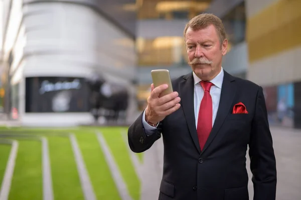 Handsome senior zakenman met snor met behulp van telefoon in de stad — Stockfoto