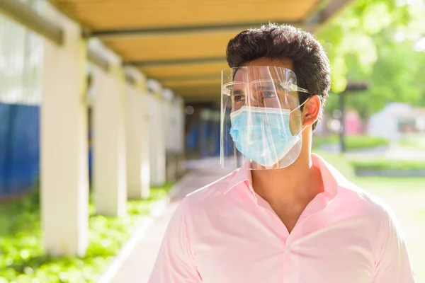Portrait of young Indian businessman with mask and face shield for protection from corona virus outbreak at the park outdoors