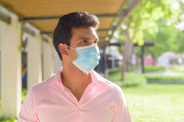 Portrait of young Indian businessman with mask for protection from corona virus outbreak at the park outdoors