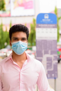 Portrait of young Indian businessman with mask for protection from corona virus outbreak at the bus stop in the city