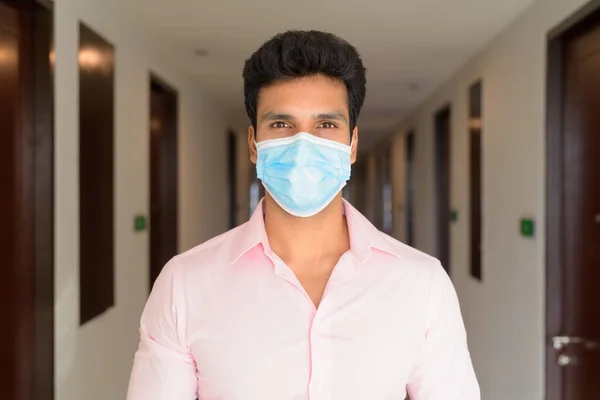 Portrait of young Indian businessman with mask for protection from corona virus outbreak in the corridor