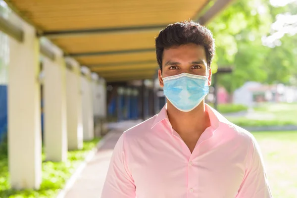 Portrait of young Indian businessman with mask for protection from corona virus outbreak at the park outdoors