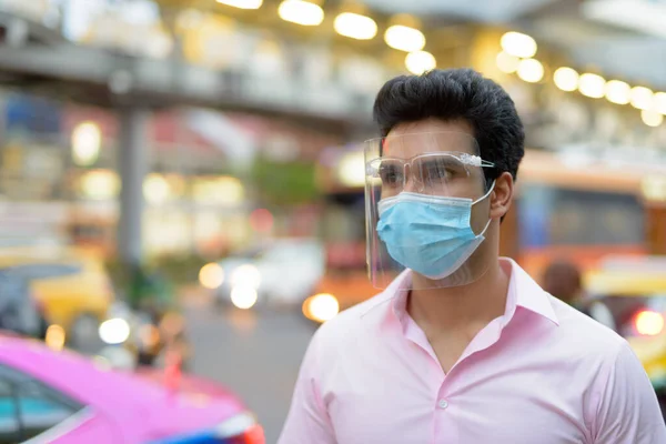 Portrait of young Indian businessman with mask and face shield for protection from corona virus outbreak in the city streets outdoors