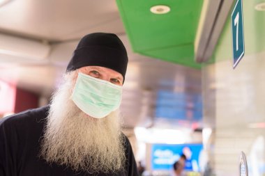Portrait of mature bearded hipster man with mask for protection from corona virus outbreak social distancing at the skytrain station