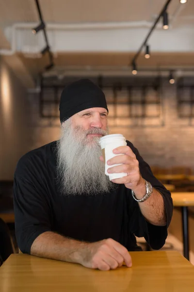 Portrait of mature handsome bearded hipster man relaxing inside the coffee shop