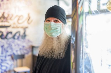 Portrait of mature bearded hipster man with mask for protection from corona virus outbreak relaxing inside the coffee shop
