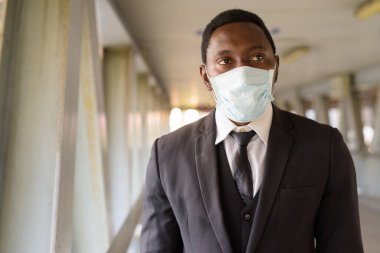 Portrait of African businessman with mask for protection from corona virus outbreak at the footbridge in the city