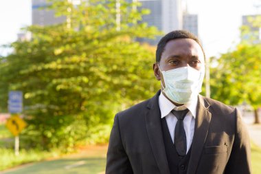 Portrait of African businessman with mask for protection from corona virus outbreak at the park in the city outdoors