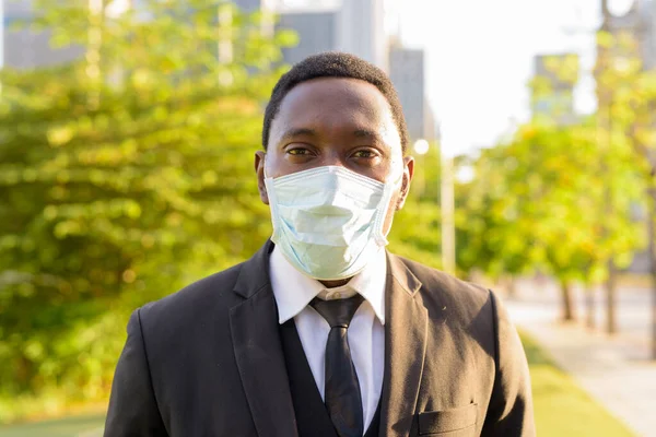 Portrait of African businessman with mask for protection from corona virus outbreak at the park in the city outdoors