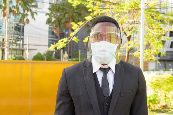 Portrait of African businessman with mask for protection from corona virus outbreak at the bus stop in the city outdoors