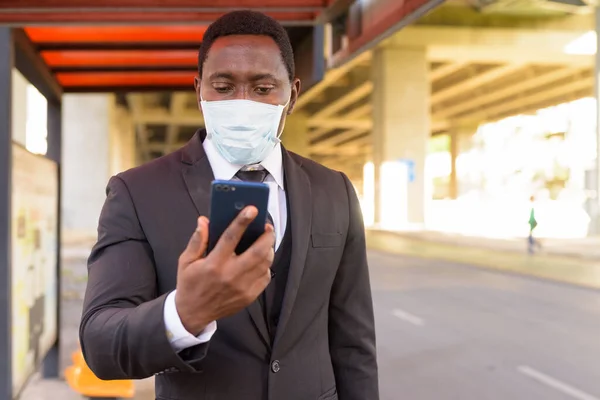 Portrait of African businessman with mask for protection from corona virus outbreak at the bus stop in the city outdoors