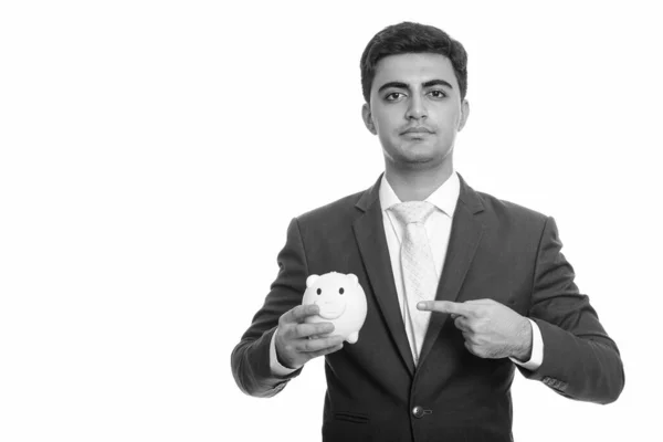 Young handsome Persian businessman holding piggy bank and pointing finger — Stock Photo, Image