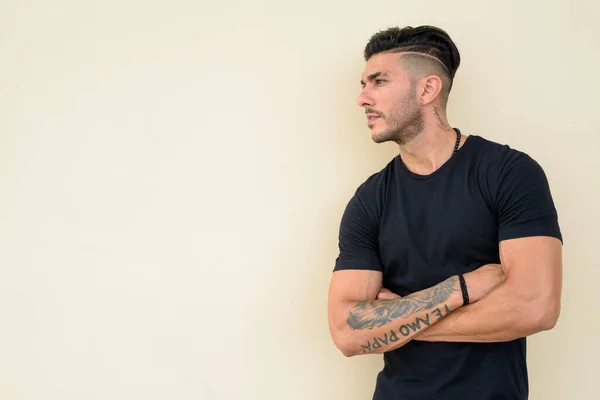 Kollarını kavuşturarak düşünen yakışıklı, sakallı, İranlı bir adamın profili.