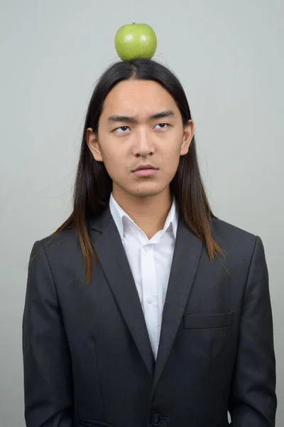 Young Asian businessman with long hair looking at apple on top of head — Stock Photo, Image