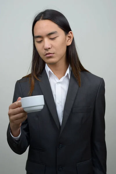 Молодий азіатський бізнесмен з довгим волоссям, що дивиться на чашку кави. — стокове фото