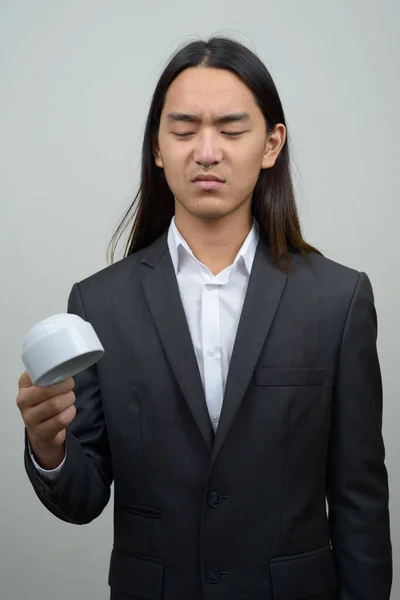 Stressé jeune homme d'affaires asiatique avec les cheveux longs tenant tasse de café à l'envers — Photo