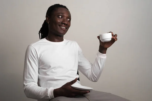 Glad ung vacker afrikansk man med dreadlocks sitter och höjer kaffe — Stockfoto