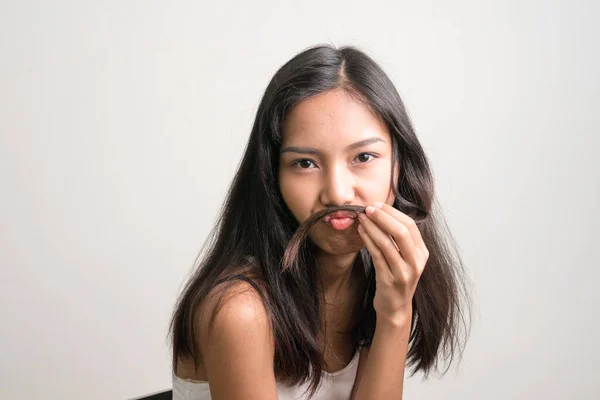 Молодая красивая азиатская девочка-подросток сидит и использует волосы в качестве усов — стоковое фото
