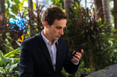 Portrait of young handsome businessman relaxing at the park outdoors