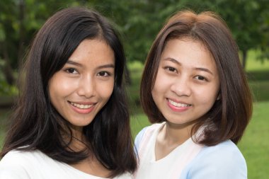 Portrait of two young Asian teenage girls as friends together relaxing at the park outdoors