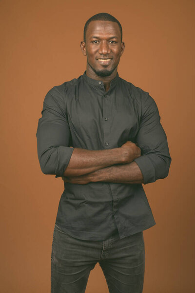 Studio shot of handsome African businessman wearing black shirt against brown background