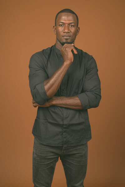 Studio shot of handsome African businessman wearing black shirt against brown background