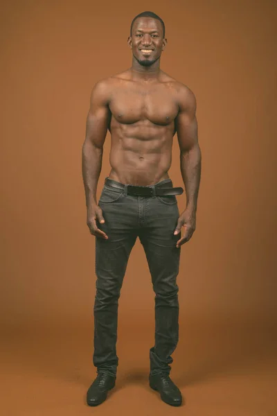 スタジオショットのハンサムな筋肉アフリカ人男性無表情に対する茶色の背景 — ストック写真