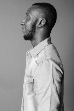 Studio shot of young handsome bearded African man with short hair against gray background in black and white