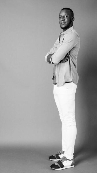 Studio shot of young handsome bearded African man with short hair against gray background in black and white